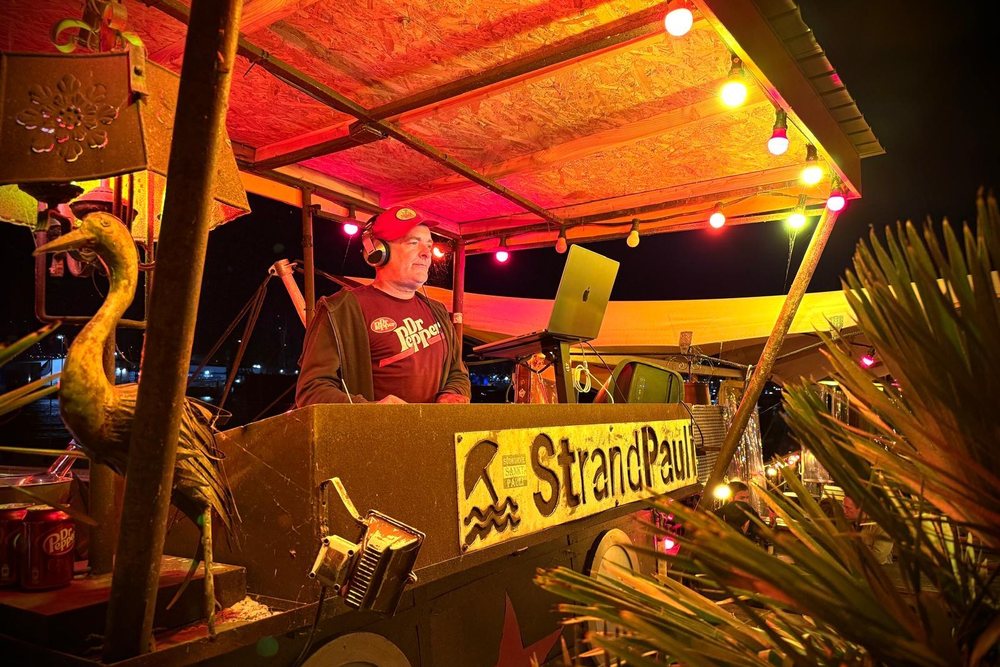 DrPepper an seinem DJ-Pult bei Nacht, StrandPauli, mit Kopfhörern und Laptop im warmen Lichterketten-Ambiente